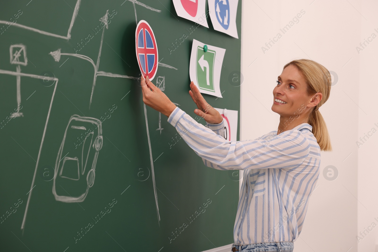 Photo of Teacher showing No Stopping road sign near chalkboard during lesson in driving school