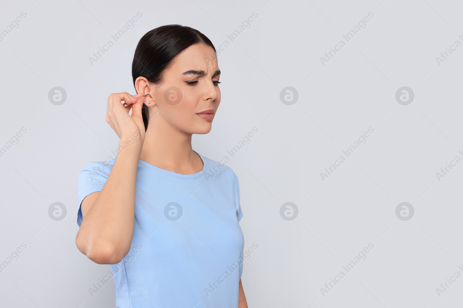 Photo of Young woman cleaning ear with cotton swab on light grey background. Space for text