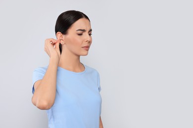 Photo of Young woman cleaning ear with cotton swab on light grey background. Space for text