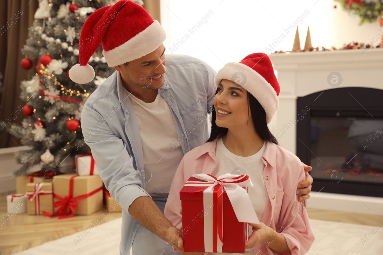 Photo of Happy couple in Santa hats with Christmas gift at home