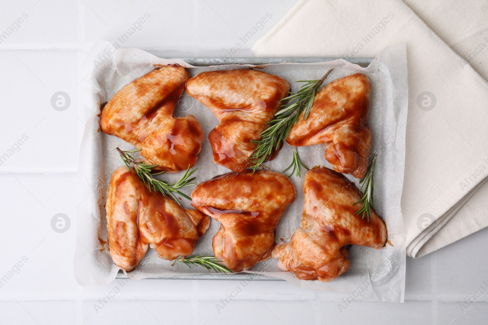 Photo of Raw marinated chicken wings and rosemary on light tiled table, top view