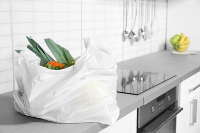 Photo of Plastic shopping bag full of vegetables on countertop in kitchen. Space for text