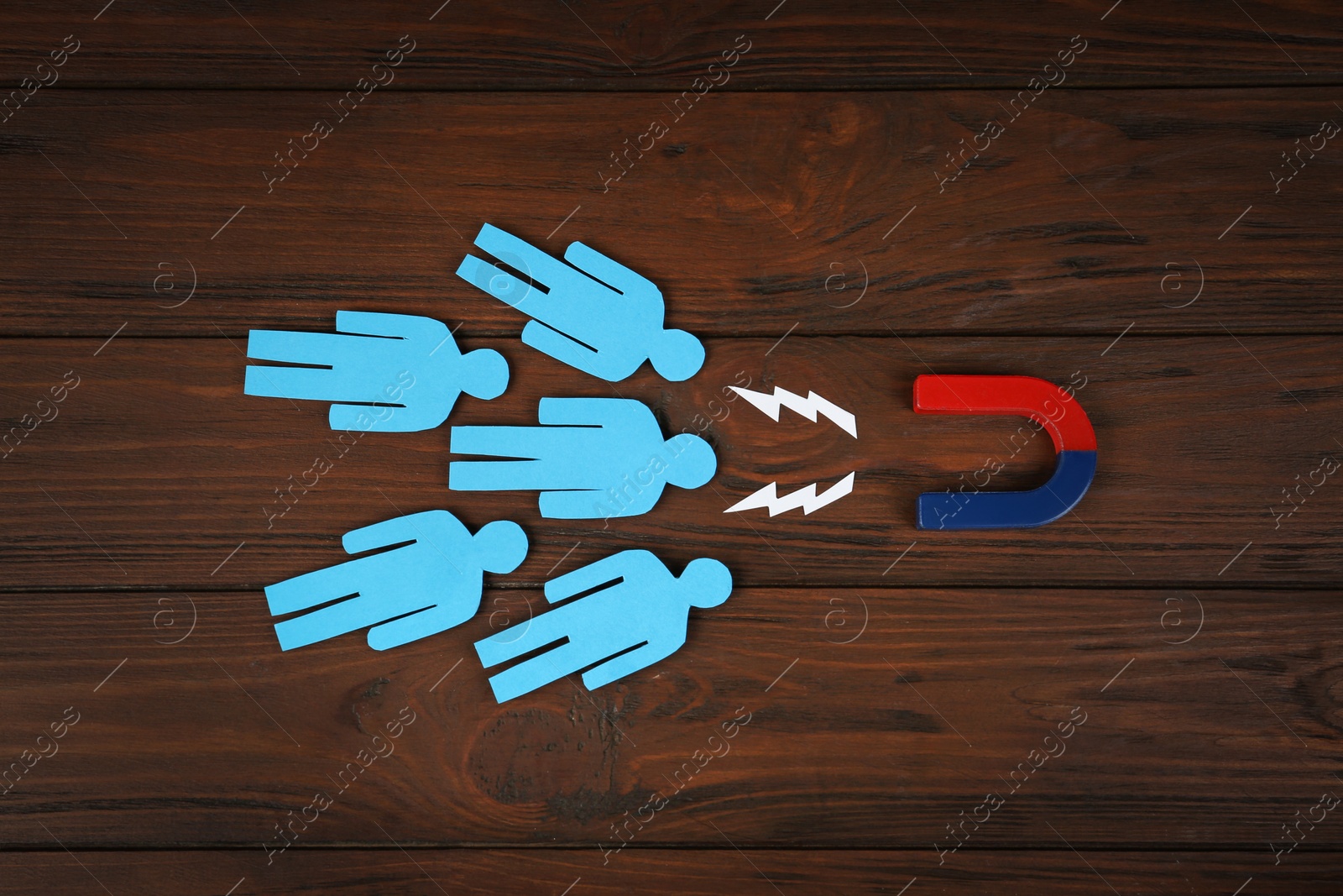 Photo of Magnet attracting paper people on wooden background, flat lay