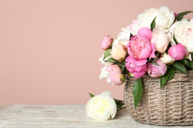 Photo of Basket with beautiful peonies on wooden table. Space for text