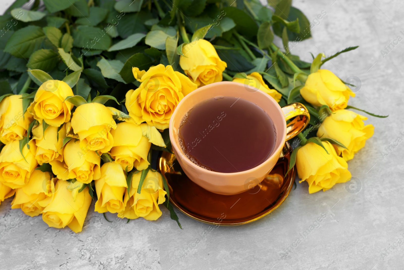 Photo of Cup of tea and beautiful yellow roses on light table, above view