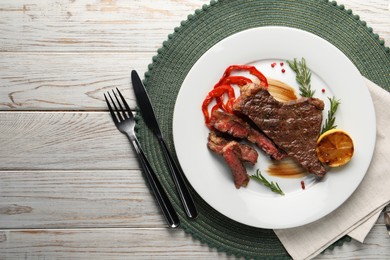 Photo of Delicious grilled beef steak with pepper and spices served on light wooden table, flat lay. Space for text