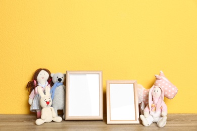 Photo of Soft toys and photo frames on table against yellow background, space for text. Child room interior