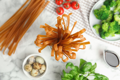 Uncooked buckwheat noodles and fresh ingredients on white marble table, flat lay