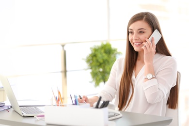 Photo of Young woman talking on phone at workplace