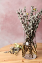 Beautiful pussy willow branches on wooden table against pink background