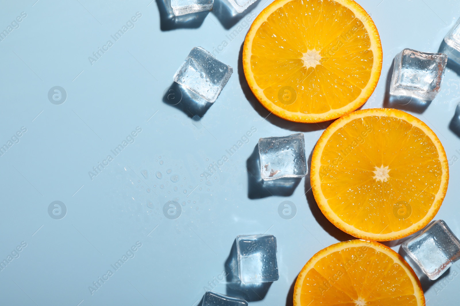 Photo of Slices of juicy orange and ice cubes on light blue background, flat lay. Space for text