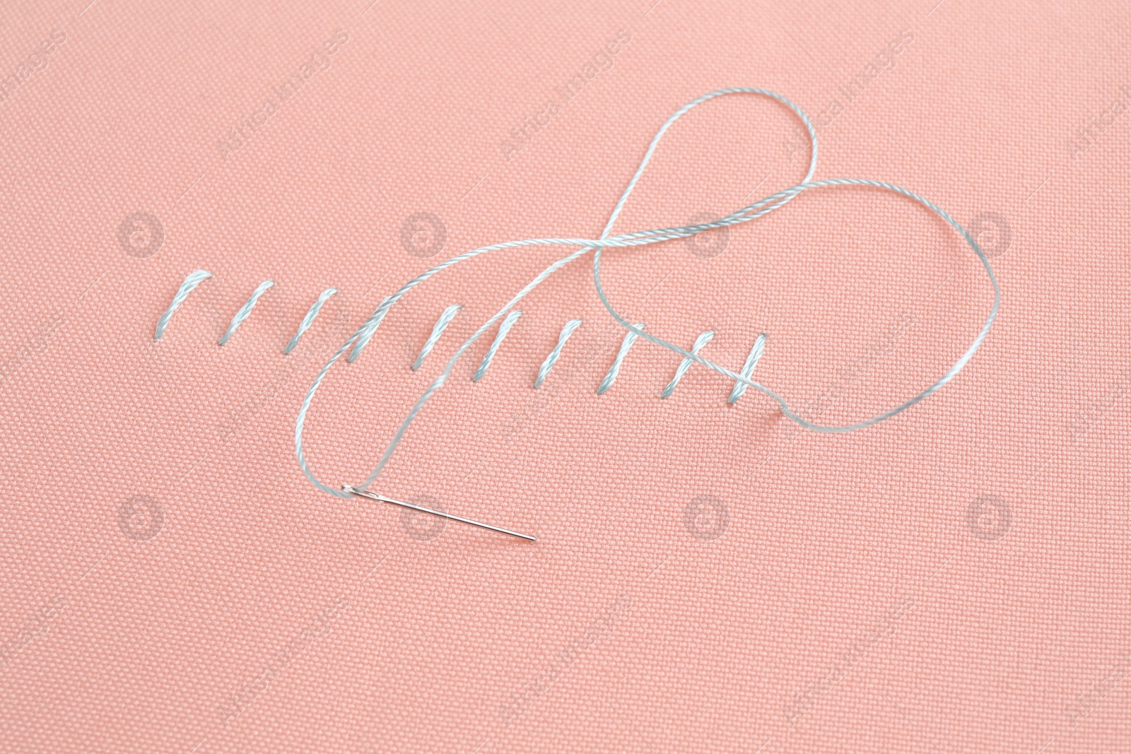 Photo of Sewing needle with thread and stitches on coral cloth, closeup