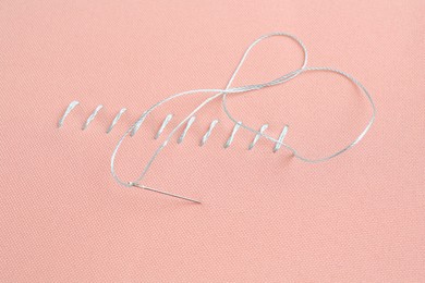 Photo of Sewing needle with thread and stitches on coral cloth, closeup