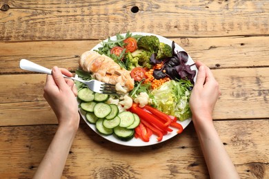 Photo of Balanced diet and healthy foods. Woman eating dinner at wooden table, above view