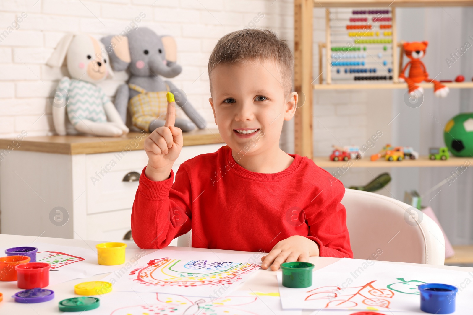 Photo of Little boy painting with finger at white table indoors