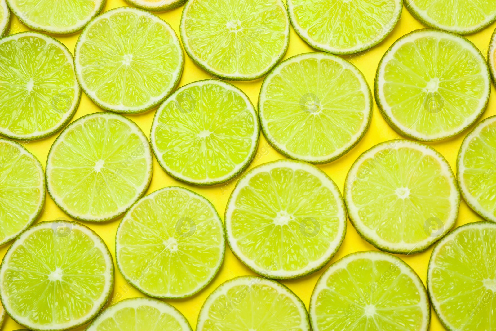 Photo of Juicy fresh lime slices on yellow background, flat lay