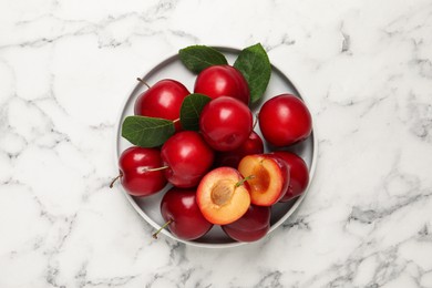 Photo of Delicious ripe cherry plums with leaves on white marble table, top view