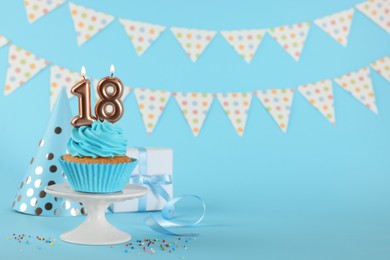 Coming of age party - 18th birthday. Delicious cupcake with number shaped candles on light blue background, space for text
