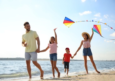 Photo of Happy parents and their children playing with kites on beach near sea. Spending time in nature