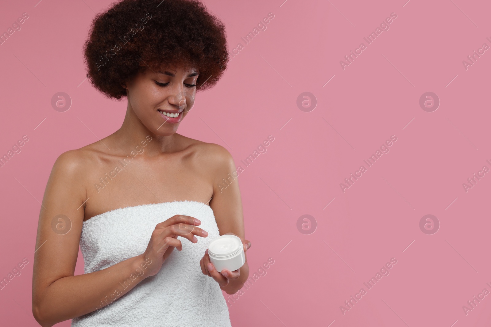 Photo of Beautiful young woman holding body cream on pink background, space for text