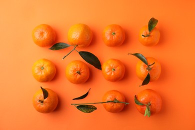 Photo of Fresh ripe tangerines with green leaves on orange background, flat lay