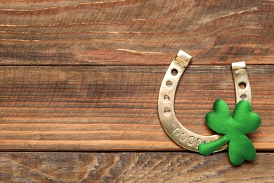 Golden horseshoe and decorative clover leaf on wooden table, flat lay with space for text. Saint Patrick's Day celebration