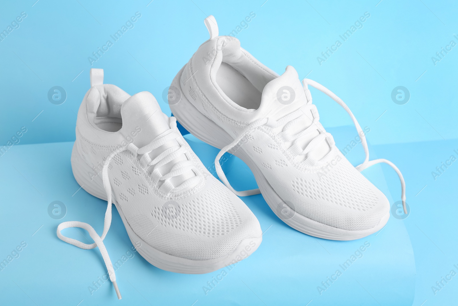 Photo of Stylish white sports shoes on light blue background