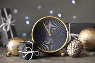 Stylish clock with decor on grey table against blurred Christmas lights, closeup. New Year countdown