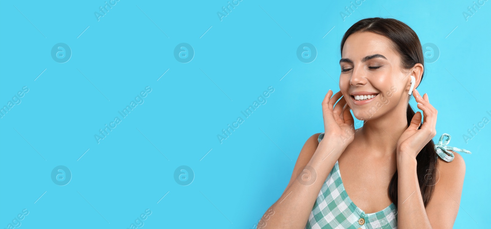 Image of Young woman listening to music with wireless earphones on turquoise background, space for text. Banner design