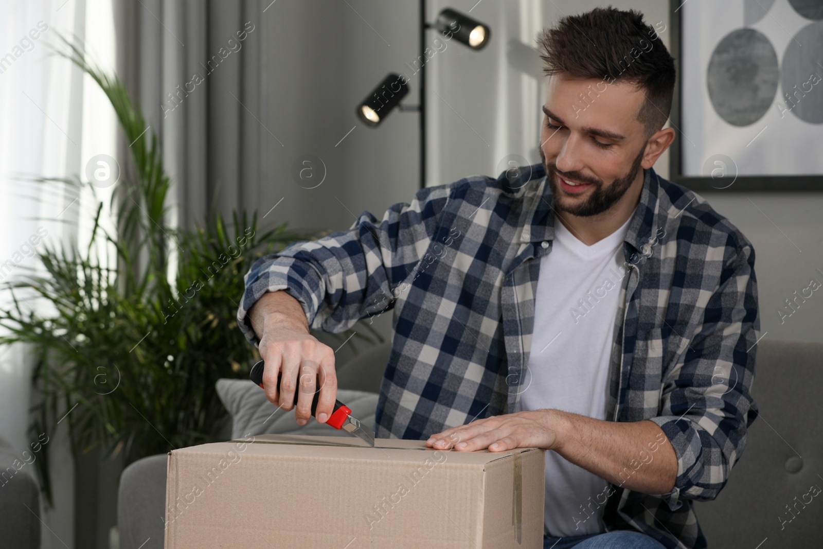 Photo of Man using utility knife to open parcel at home