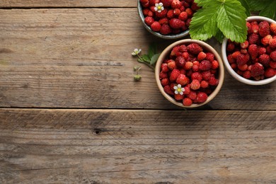 Photo of Fresh wild strawberries in bowls and leaves on wooden table, flat lay. Space for text