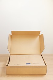 Photo of Open cardboard box with item wrapped in kraft paper on wooden table. Delivery service