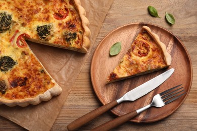 Photo of Delicious homemade vegetable quiche and cutlery on wooden table, flat lay
