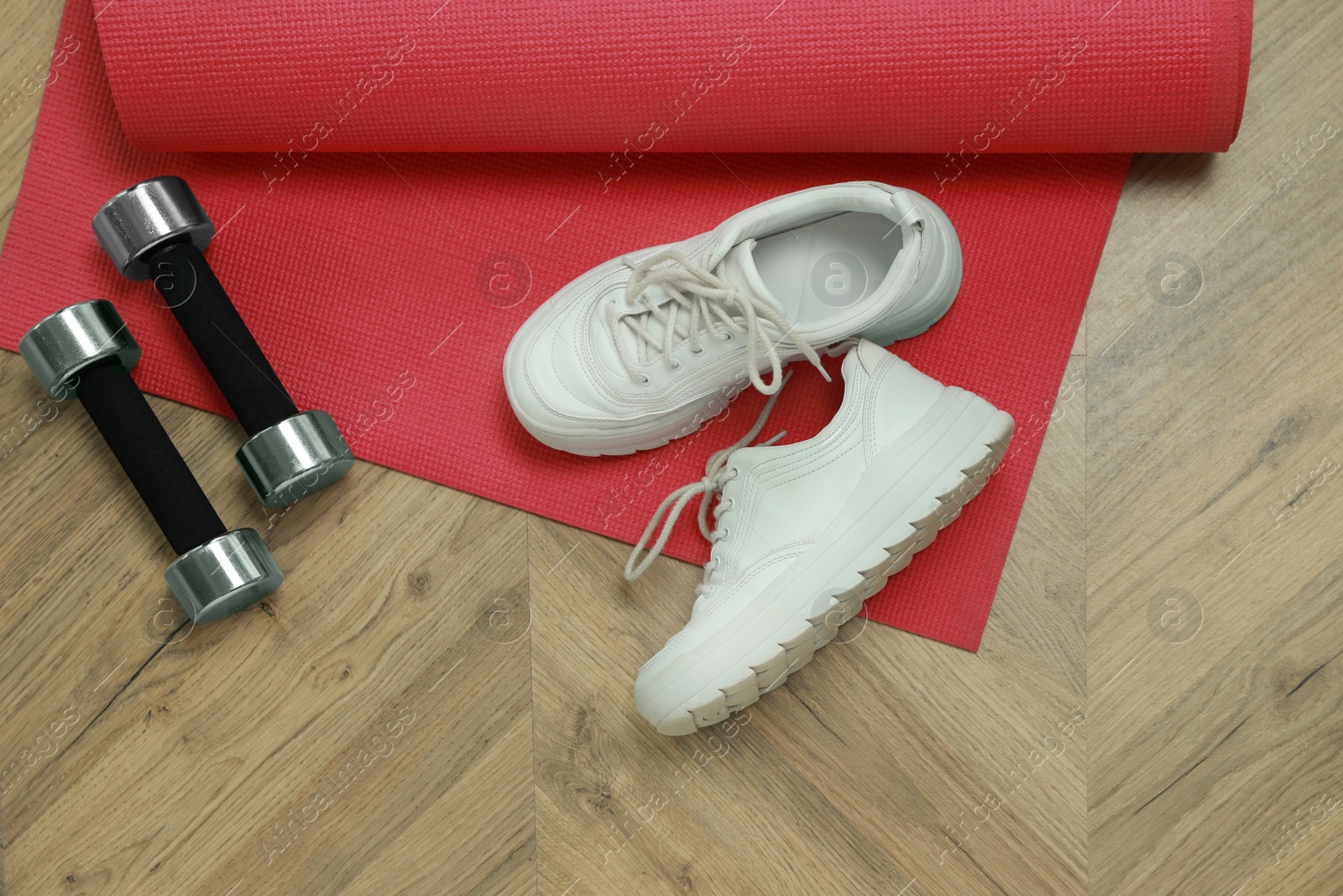 Photo of Dumbbells, sneakers and mat on wooden floor, above view