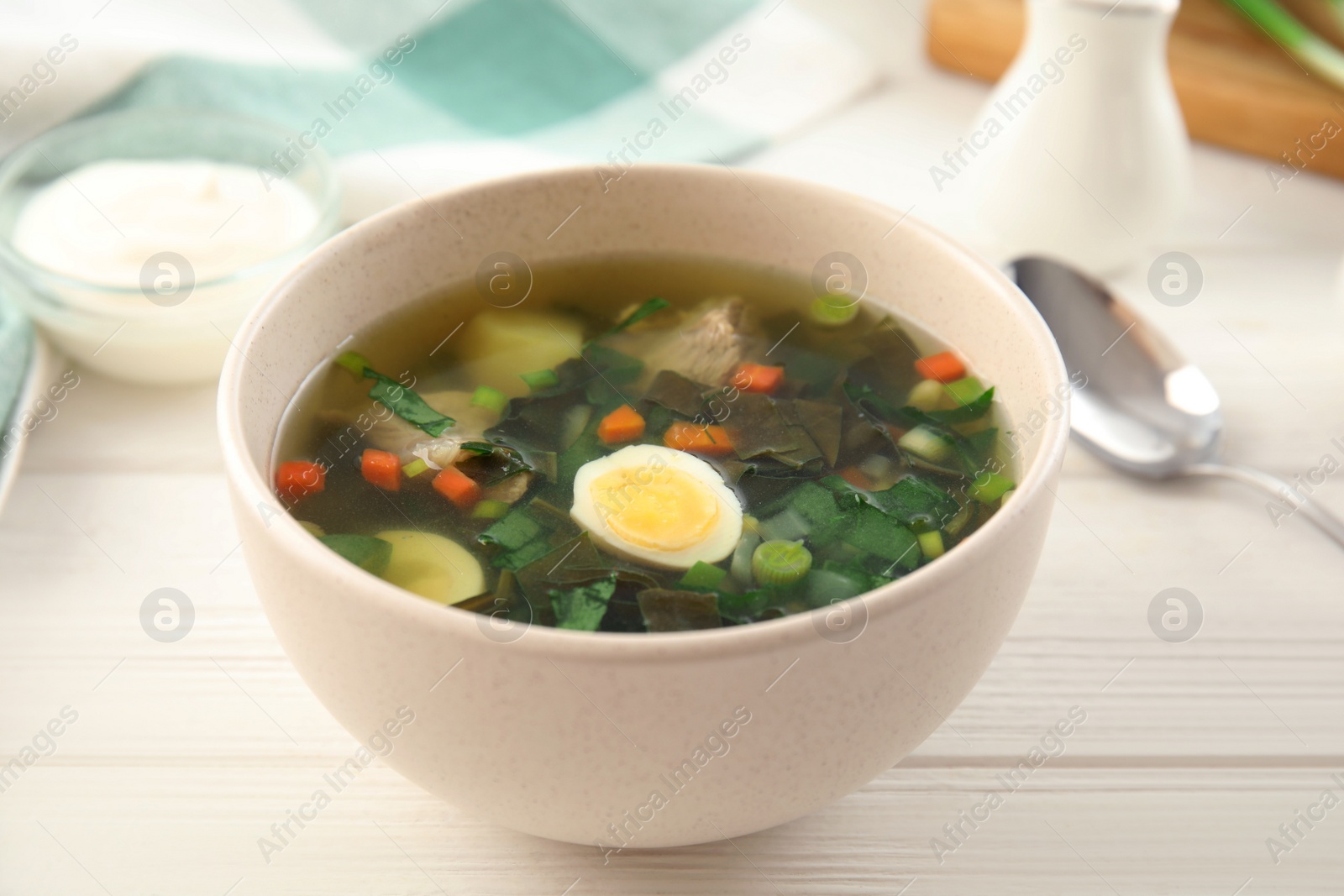 Photo of Delicious sorrel soup with meat and egg served on white wooden table