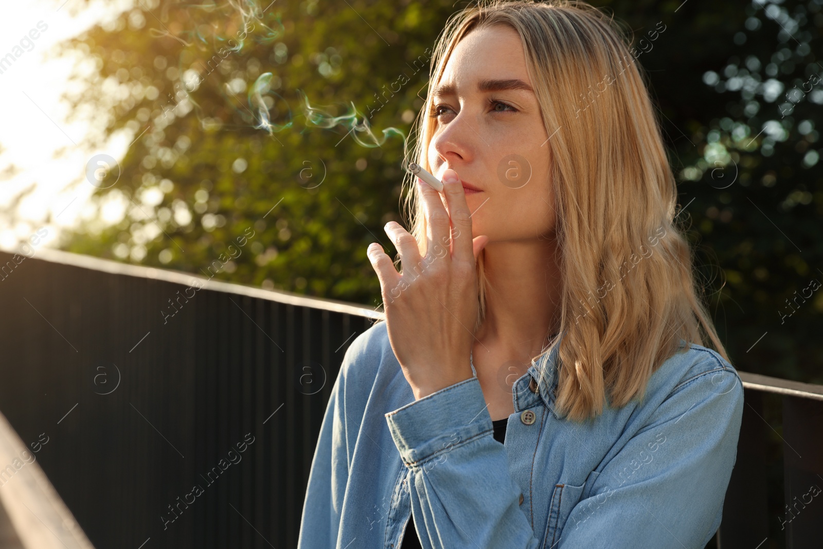 Photo of Young woman smoking cigarette outdoors, space for text