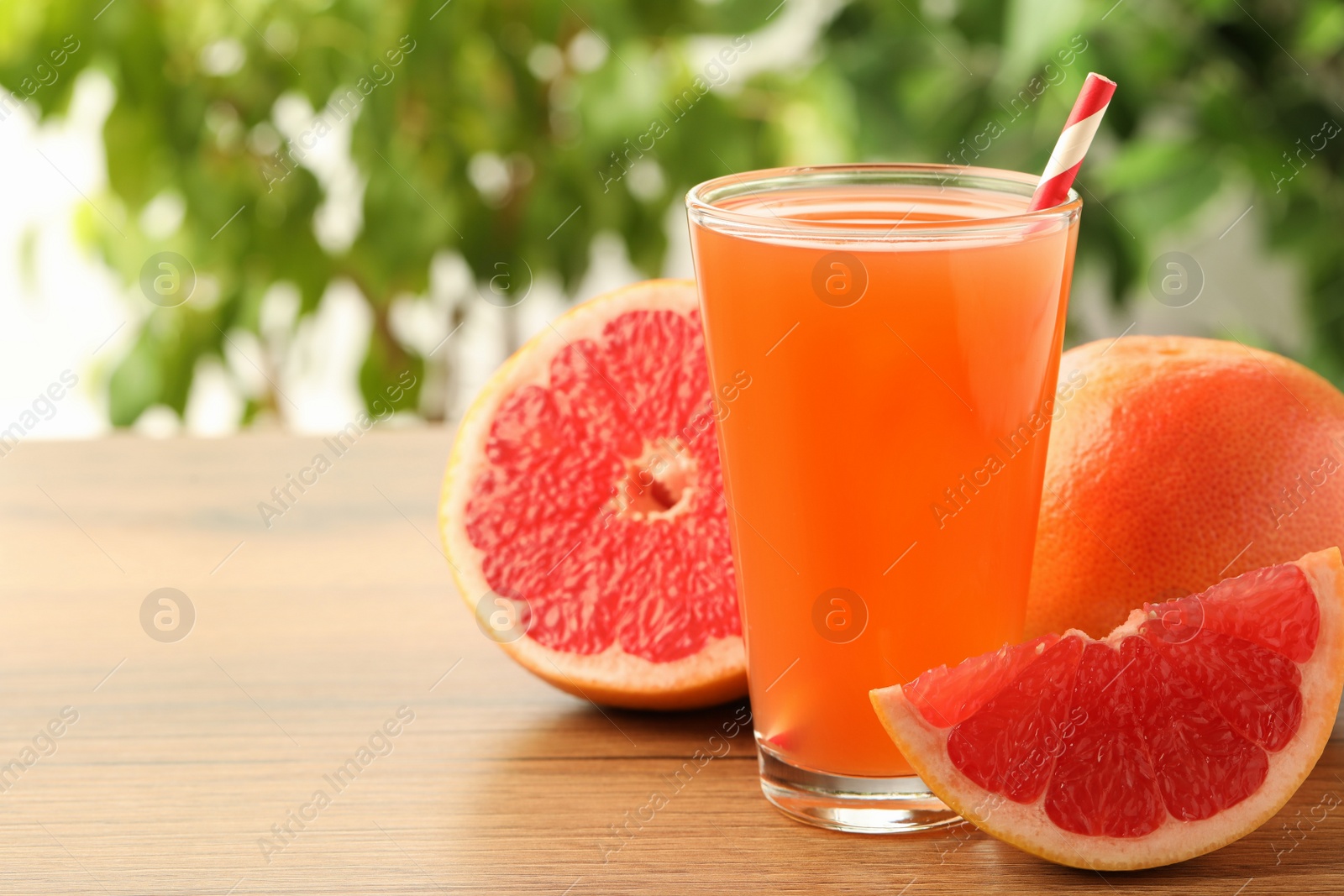 Photo of Glass of delicious grapefruit juice on wooden table against blurred background, space for text