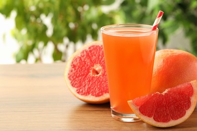 Glass of delicious grapefruit juice on wooden table against blurred background, space for text