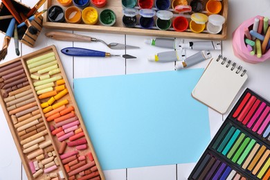Photo of Blank sheet of paper, colorful chalk pastels and other drawing tools on white wooden table, flat lay. Modern artist's workplace