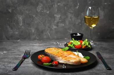 Tasty salmon steak served with glass of wine on table