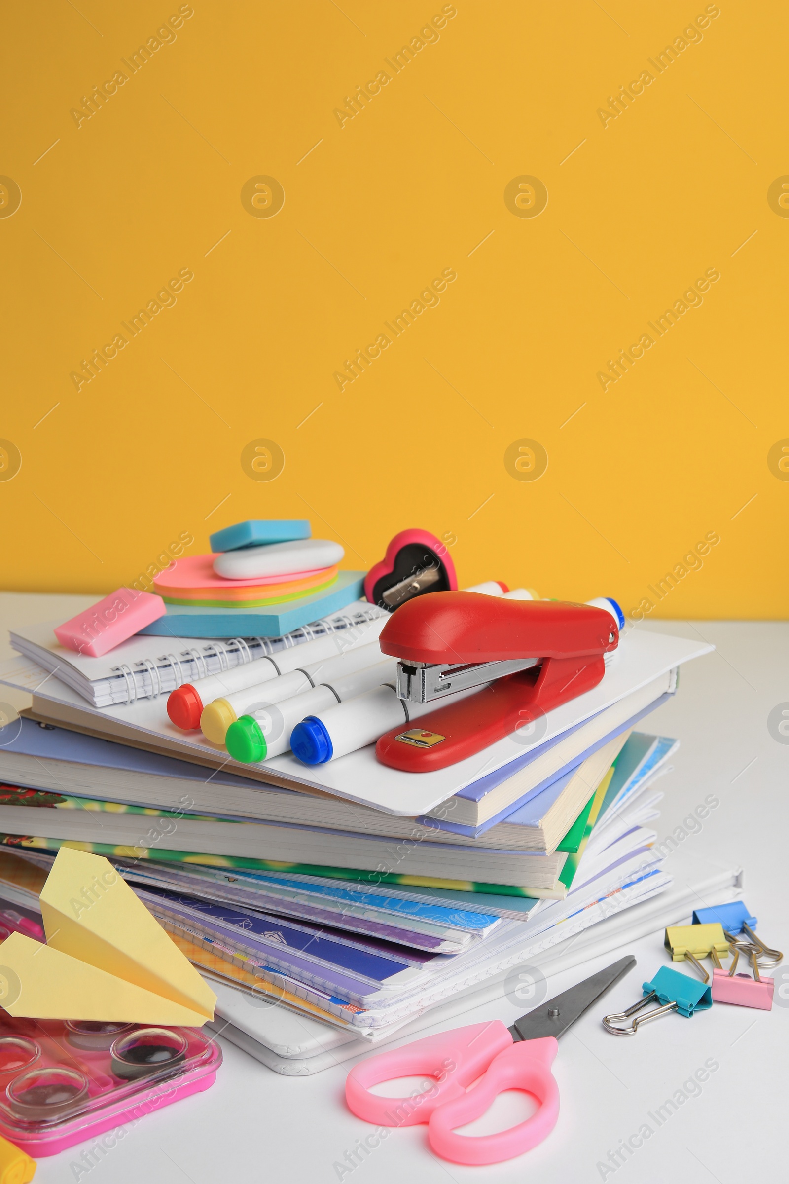 Photo of Many books, paper plane and different school stationery on white table against orange background. Back to school