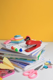 Many books, paper plane and different school stationery on white table against orange background. Back to school