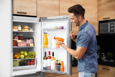 Man taking bottle with juice out of refrigerator in kitchen