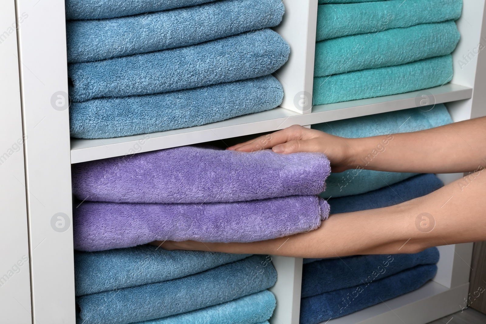 Photo of Woman putting towels on shelf, closeup view