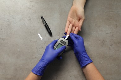 Diabetes. Doctor checking patient's blood sugar level with glucometer at gray table, top view