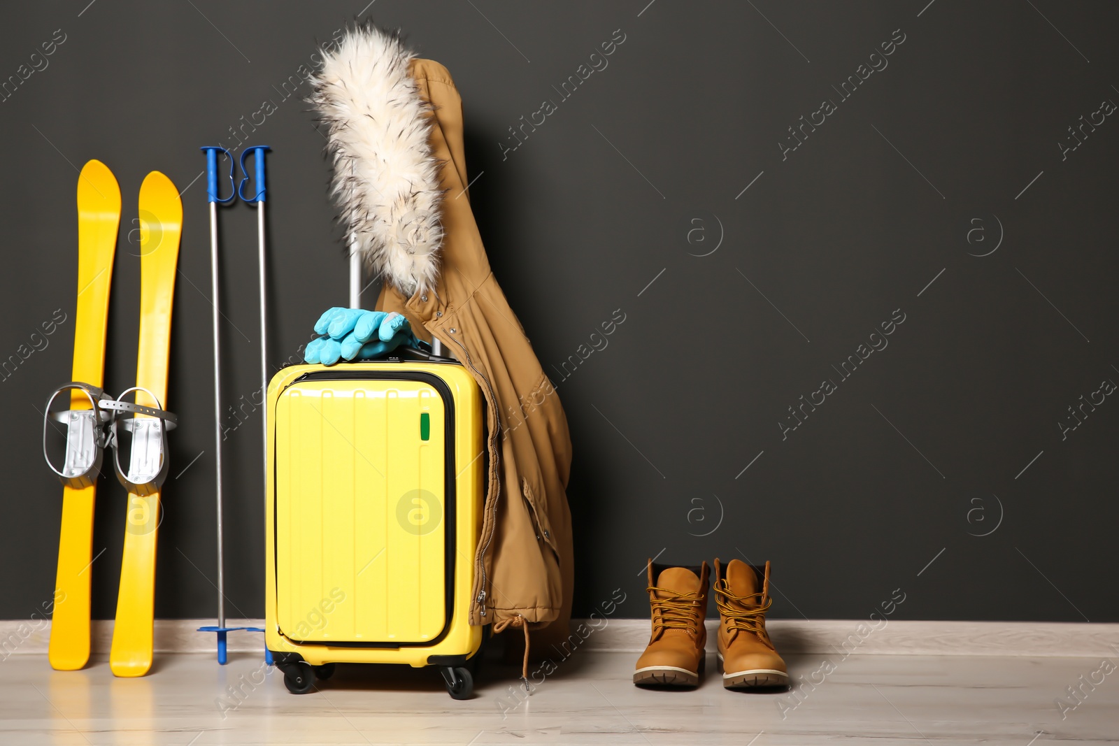 Photo of Suitcase, jacket and skis on floor against black wall, space for text. Winter vacation