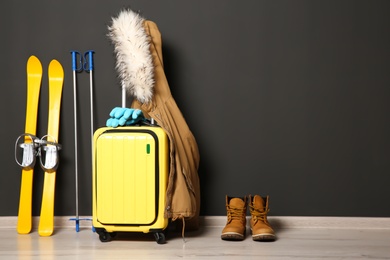 Photo of Suitcase, jacket and skis on floor against black wall, space for text. Winter vacation