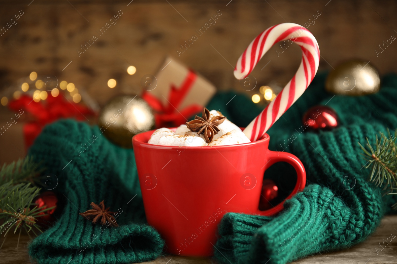 Photo of Cup of tasty cocoa with marshmallows and Christmas candy cane on wooden table against blurred festive lights
