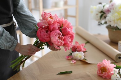 Photo of Florist making beautiful peony bouquet at table, closeup