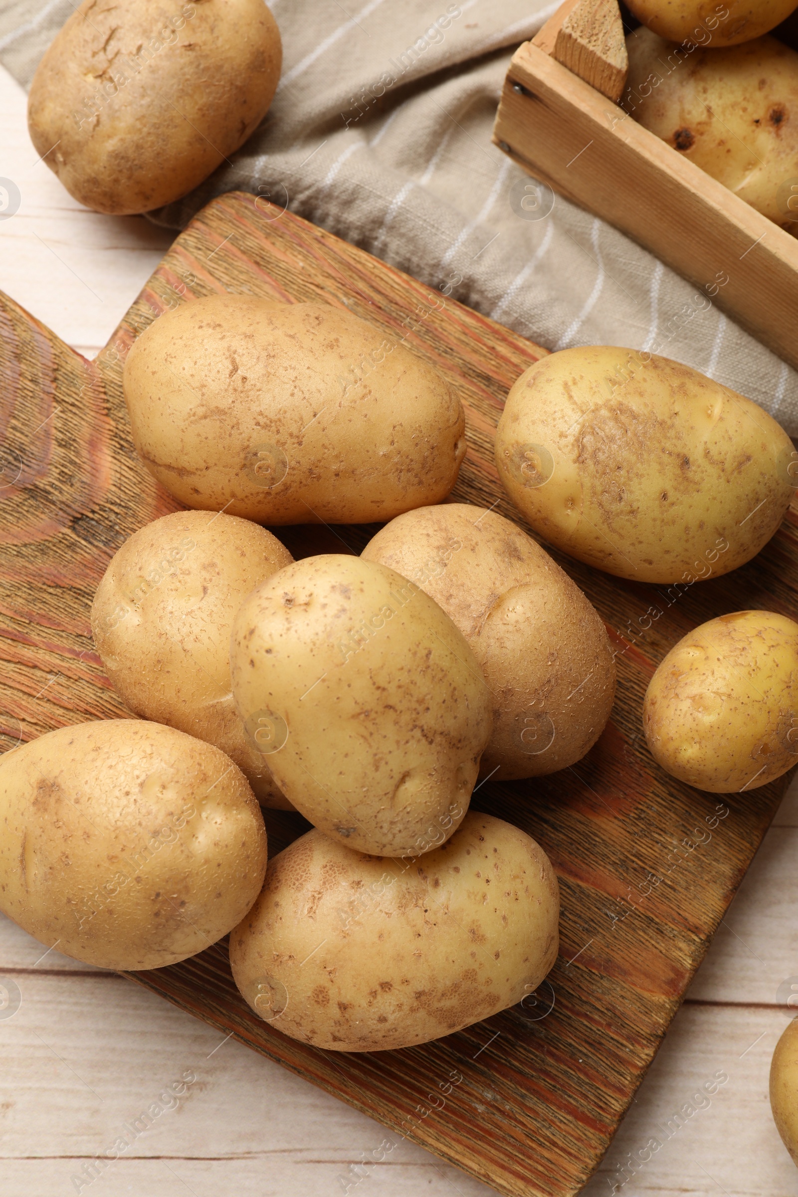 Photo of Raw fresh potatoes and cutting board on light wooden table, top view